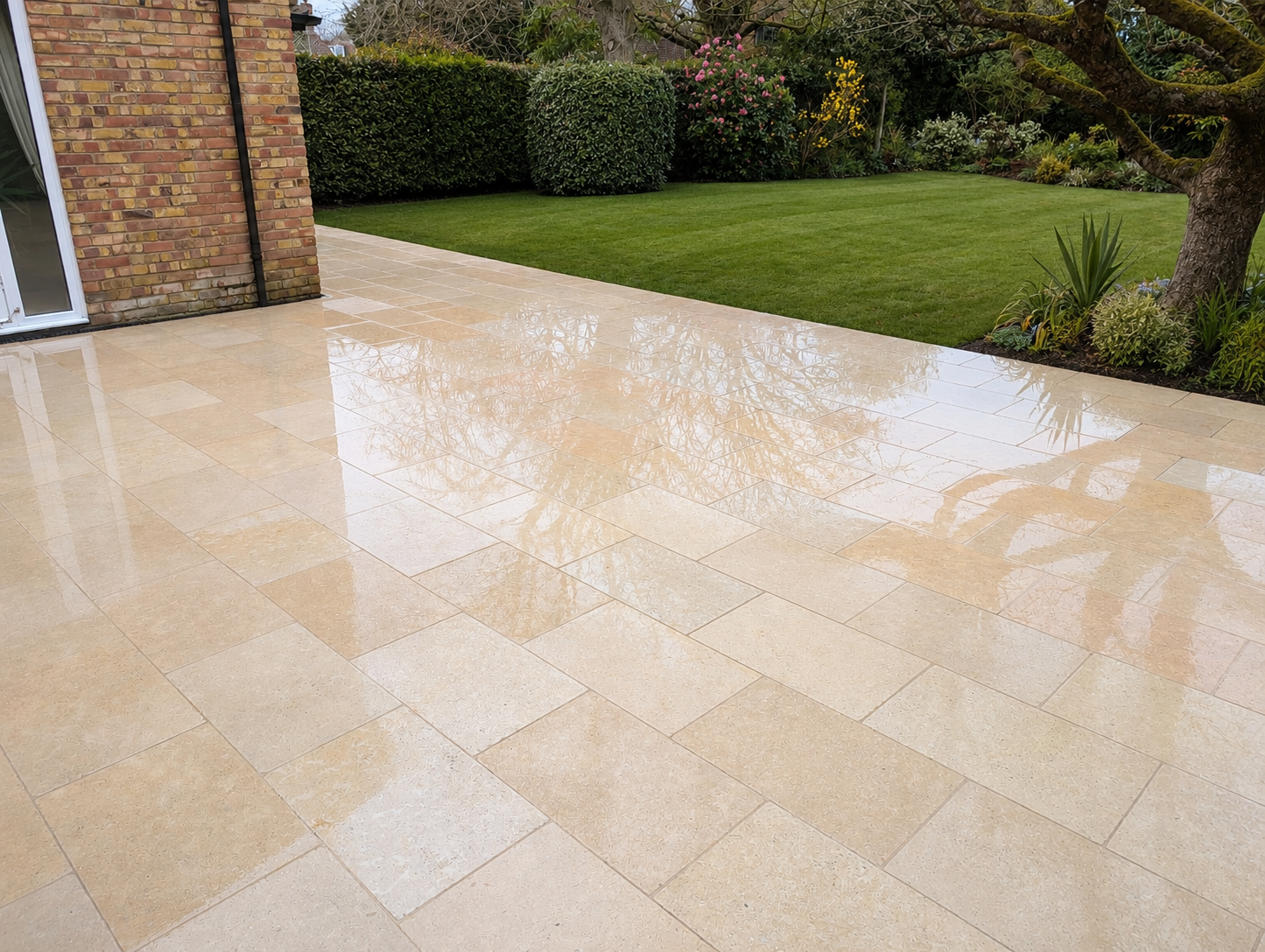 Freshly cleaned cream limestone patio with a mirror-like wet finish, backing onto a manicured lawn in Oxfordshire